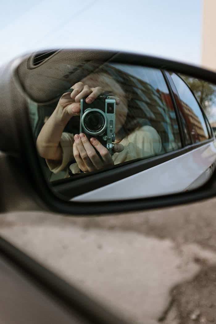 Persona fotografiando el espejo lateral de un taxi haciendo autoretrato